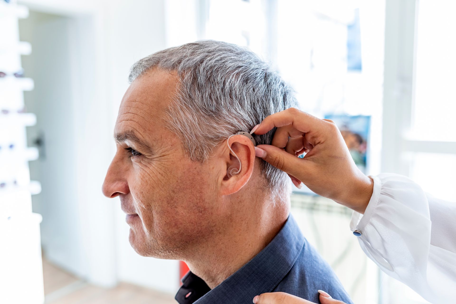 A hearing care professional fitting a behind-the-ear hearing aid for an older man